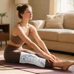 Woman in brown sports bra and leggings sitting on a yoga mat with a towel in a living room.